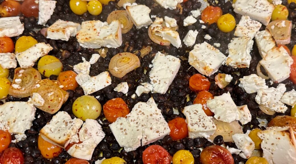 Close-up picture of finished product, showing black garbanzo beans, lightly browned feta, and roasted red, yellow and orange cherry tomatoes