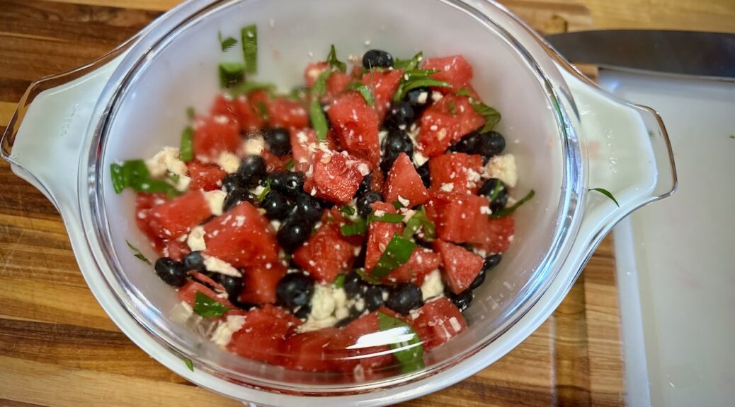 Watermelon, Blueberry and Basil Salad, with Feta, in a covered Pyrex, on a wood cutting board